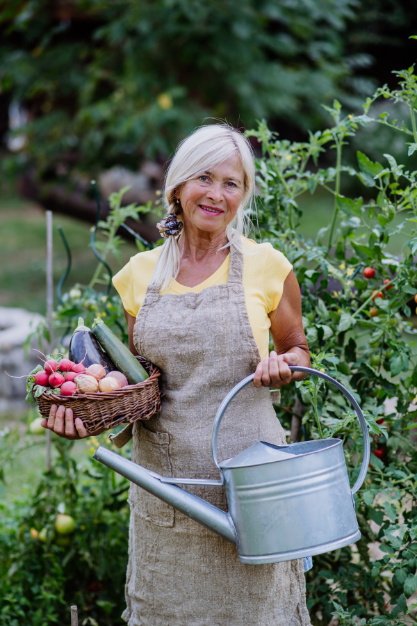 a Happy senior farmer holding basket with autumn harvest from her garden.