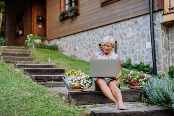 A senior woman using laptop and handling orders of her homegrown organic flowers and vegetables in garden