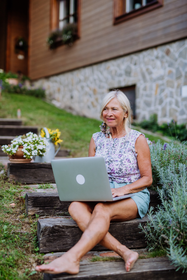 A senior woman using laptop and handling orders of her homegrown organic flowers and vegetables in garden