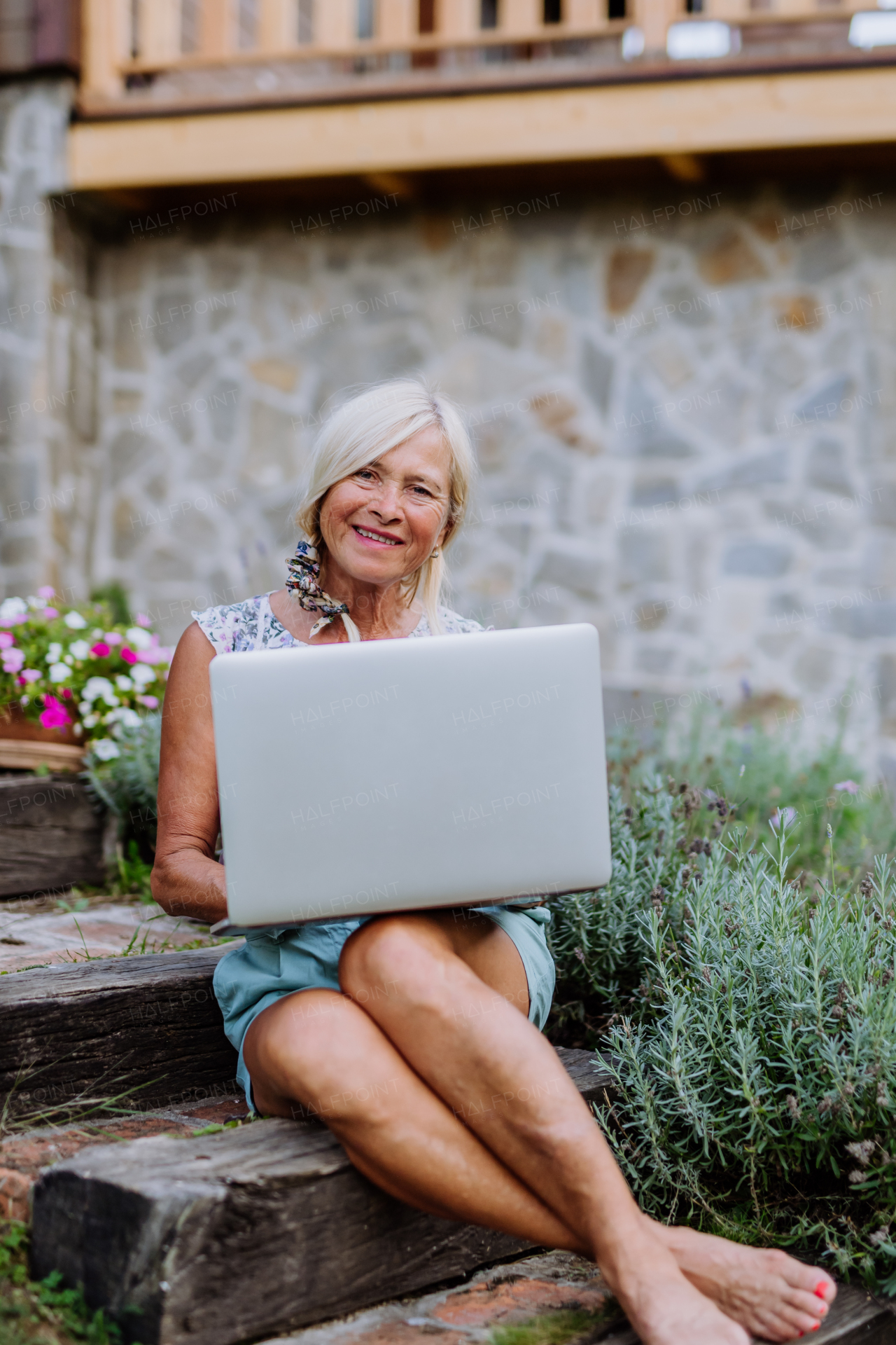 A senior woman using laptop and handling orders of her homegrown organic flowers and vegetables in garden