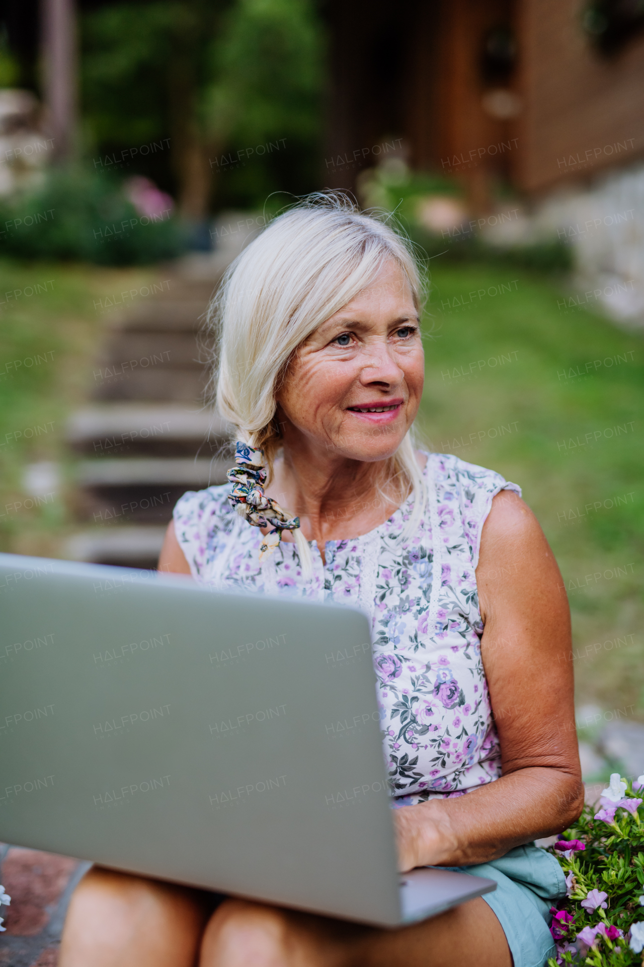 A senior woman using laptop and handling orders of her homegrown organic flowers and vegetables in garden