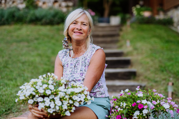 A senior woman in garden at home with her flowers.