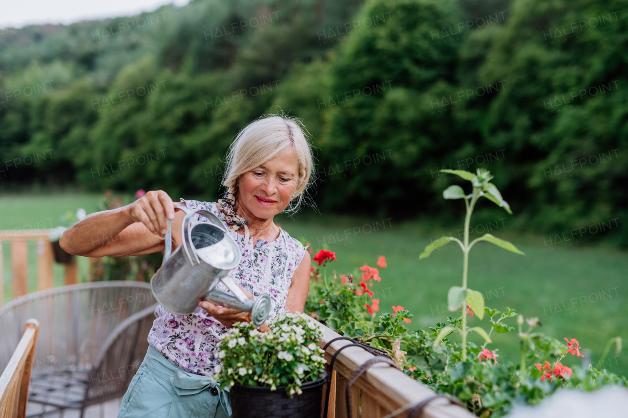 Senior woman watering flowers on terrace and enjoying view at forest.