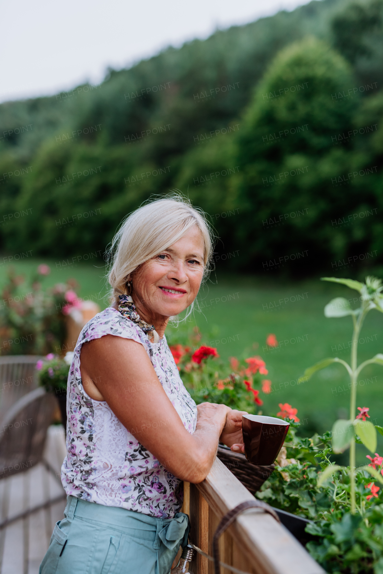 Senior woman resting on her terrace with a cup of coffee and enjoying view at forest.