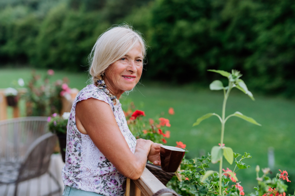 Senior woman resting on her terrace with a cup of coffee and enjoying view at forest.