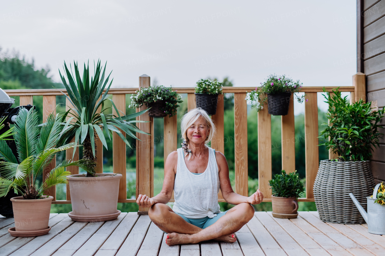 Senior woman sitting outdoors on a terrace in summer, doing yoga exercise.