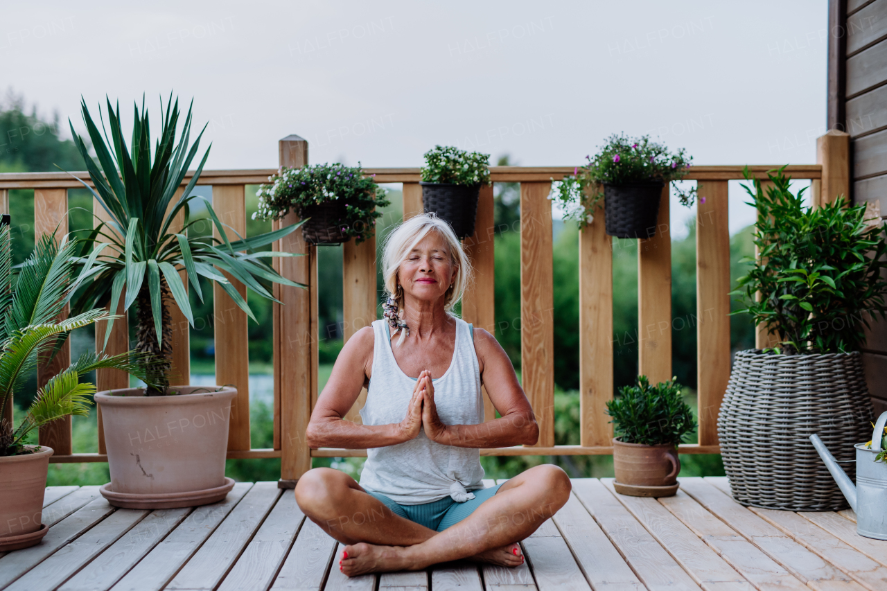 Senior woman sitting outdoors on a terrace in summer, doing yoga exercise.