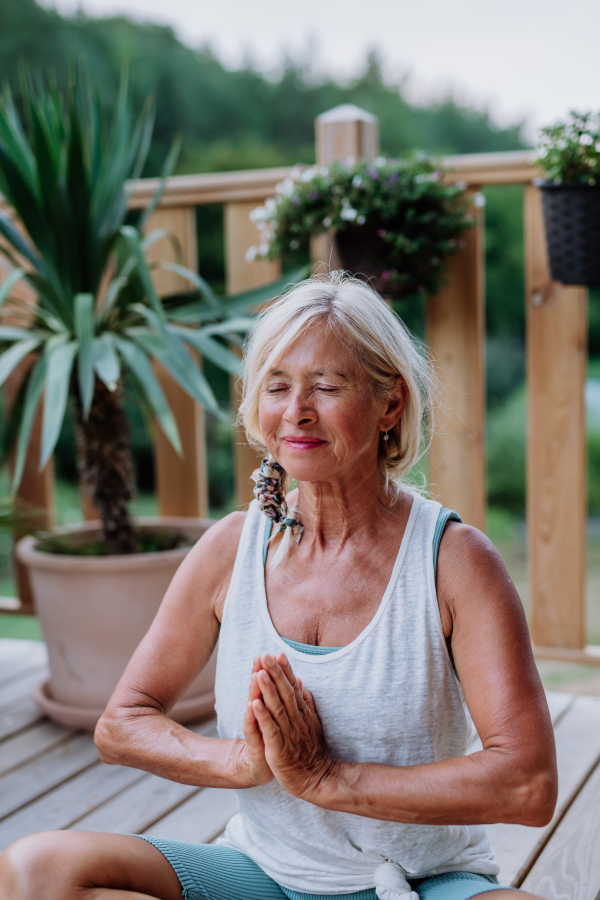 Senior woman sitting outdoors on a terrace in summer, doing yoga exercise.