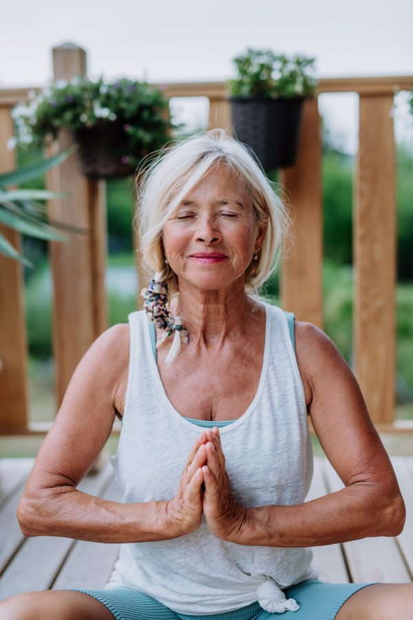 Senior woman sitting outdoors on a terrace in summer, doing yoga exercise.