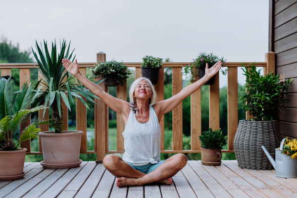 Senior woman sitting outdoors on a terrace in summer, doing yoga exercise.