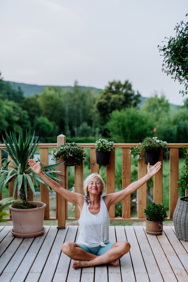 Senior woman sitting outdoors on a terrace in summer, doing yoga exercise.