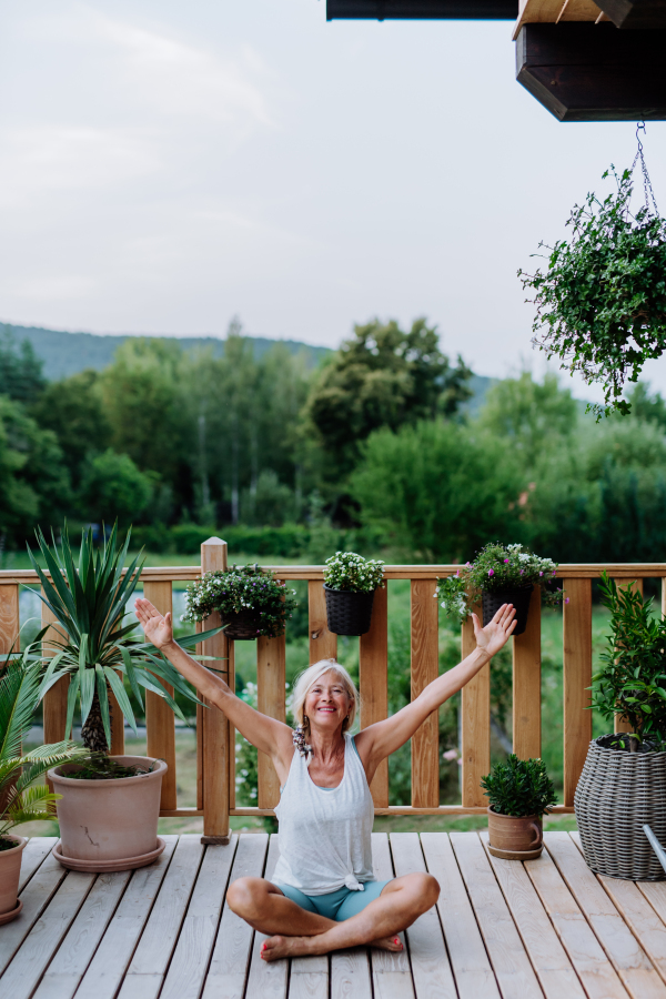 Senior woman sitting outdoors on a terrace in summer, doing yoga exercise.