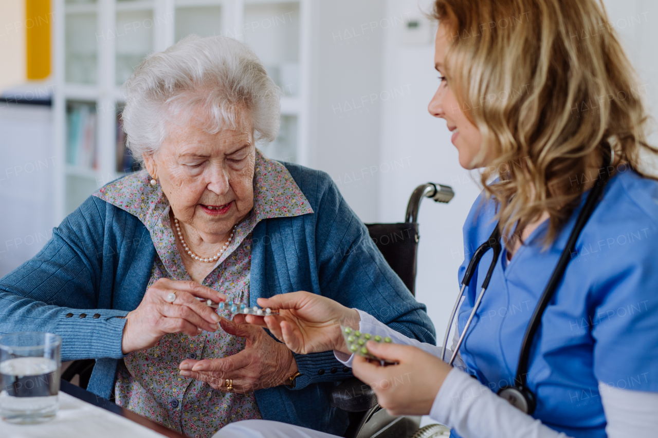 Nurse giving pills to senior woman in her home.