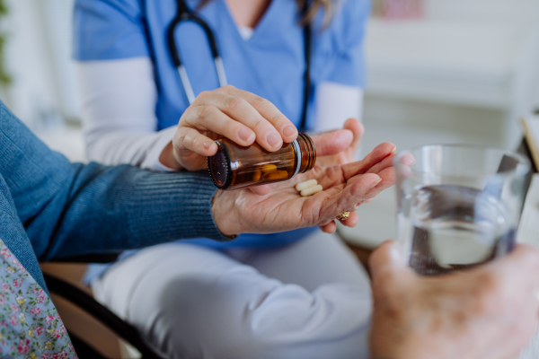 Close up of nurse giving pills to senior woman in her home.