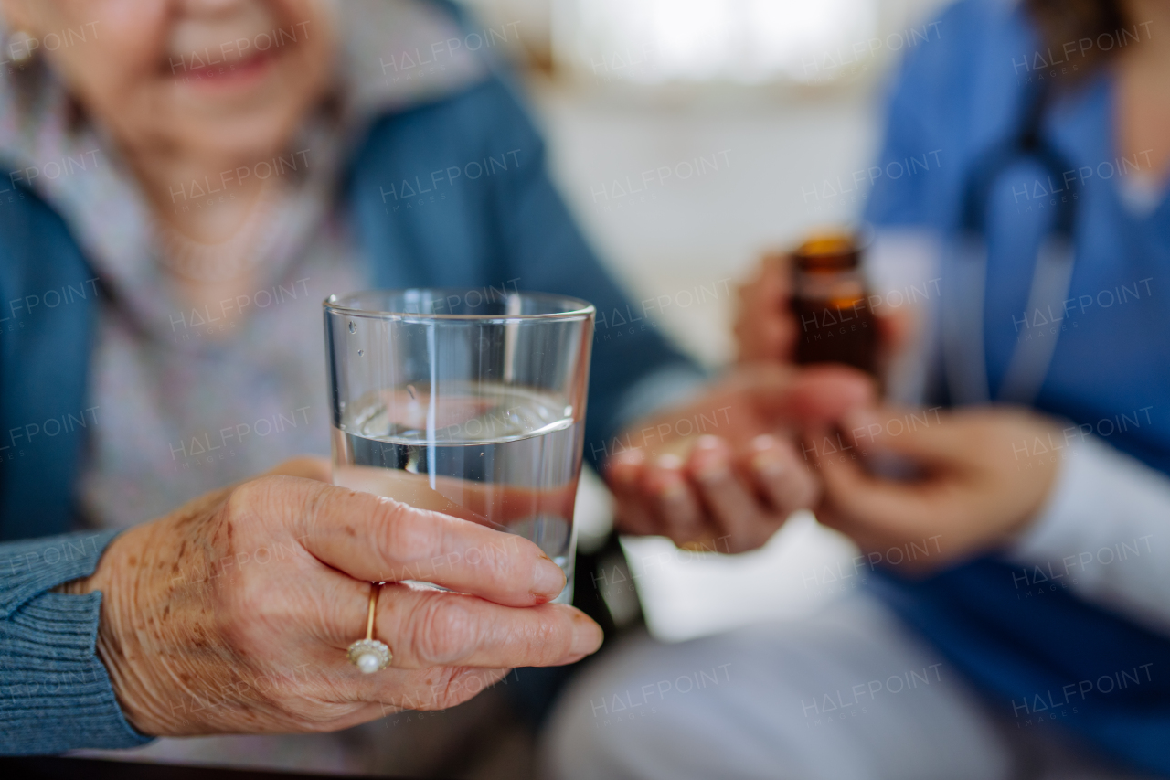 Close-up of nurse giving pills to senior woman in her home.