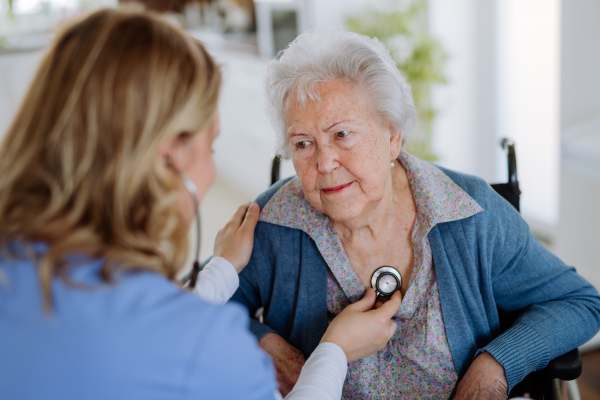 Nurse examining senior patient with stethoscope at home.