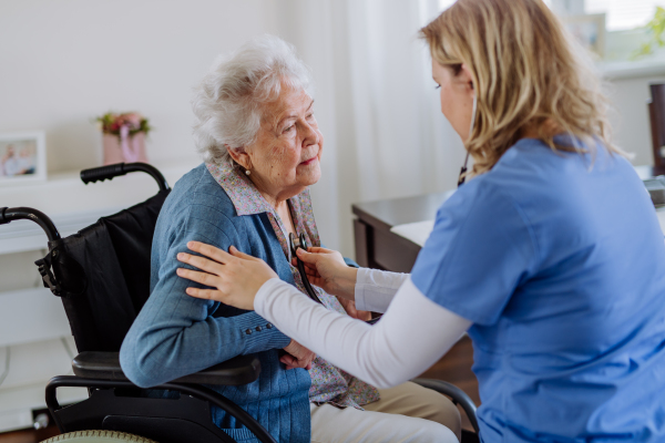 Nurse examining senior patient with stethoscope at home.