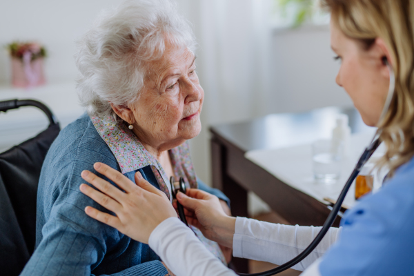 Nurse examining senior patient with stethoscope at home.