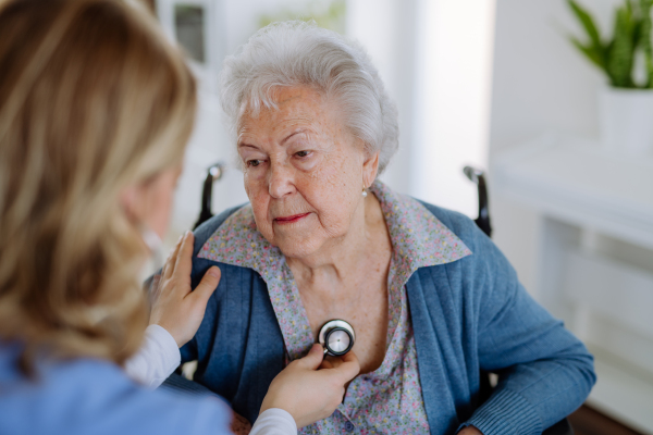 Nurse examining senior patient with stethoscope at home.