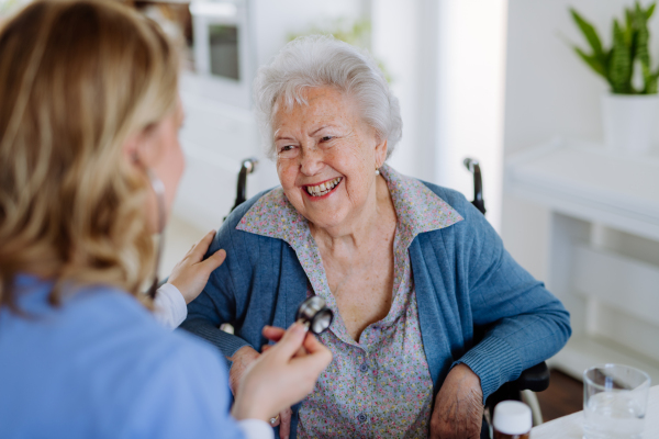 Nurse examining senior patient with stethoscope at home.