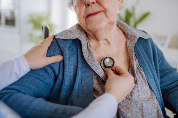 Nurse examining senior patient with stethoscope at home.