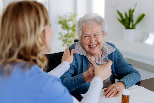 Nurse giving pills to senior woman in her home.