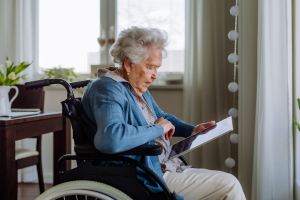 Senior woman on a wheelchair scrolling digital tablet.