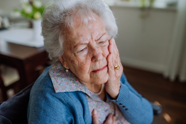 Senior woman having teeth ache, sitting in the apartment.