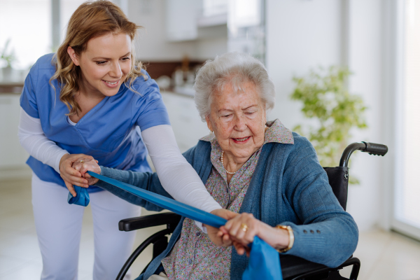 Nurse exercising with senior woman at her home, concept of a healthcare and rehabilitation.