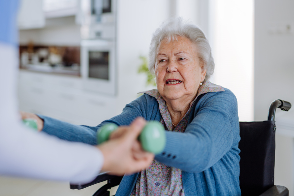 Nurse exercising with senior woman at her home, concept of a healthcare and rehabilitation.