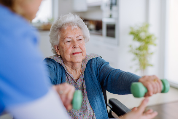 Nurse exercising with senior woman at her home, concept of a healthcare and rehabilitation.