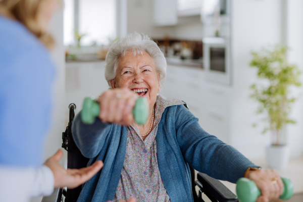 Nurse exercising with senior woman at her home, concept of a healthcare and rehabilitation.