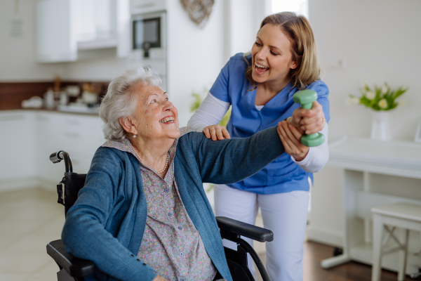 Nurse exercising with senior woman at her home, concept of a healthcare and rehabilitation.