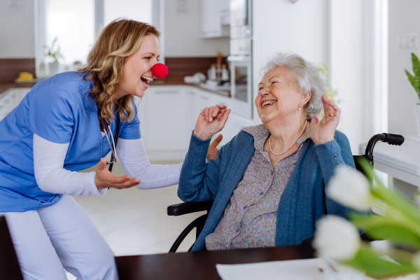 Nurse with clown nose having fun with the senior woman client.