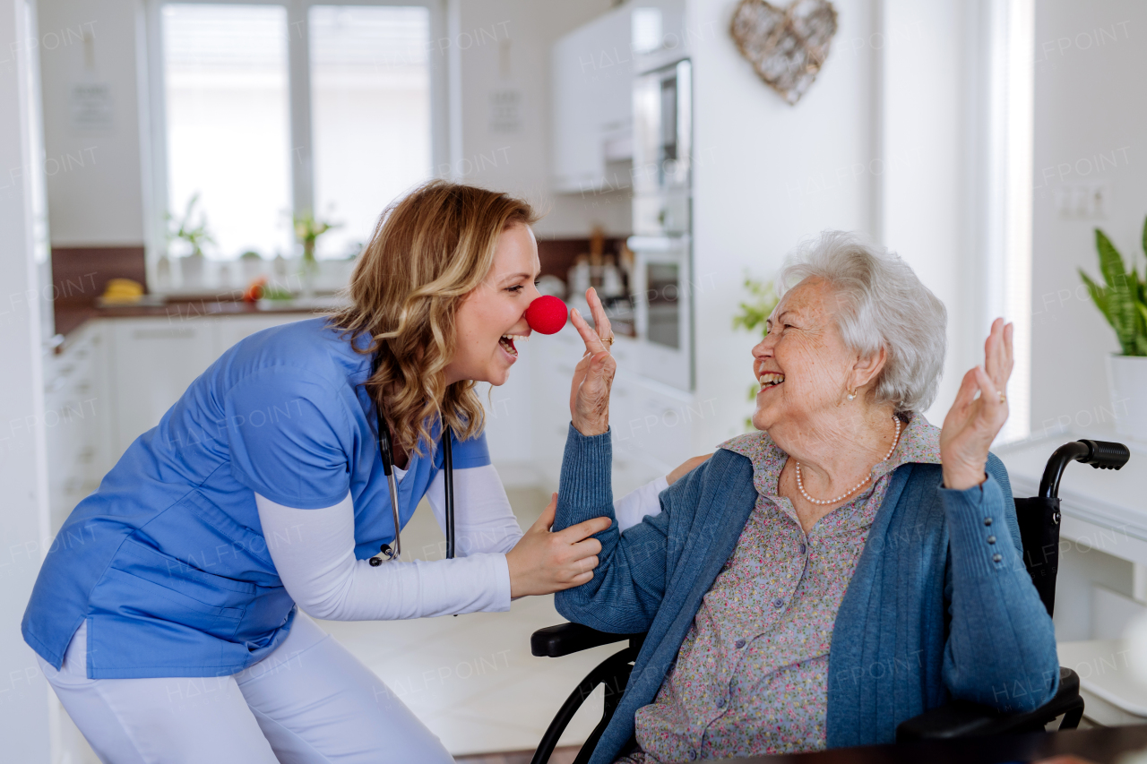 Nurse with clown nose having fun with the senior woman client.