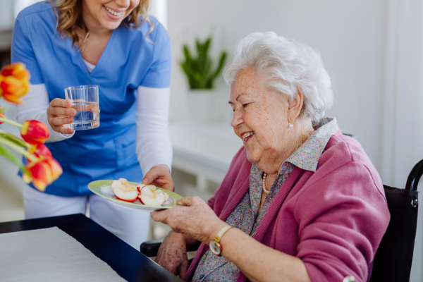 Caregiver giving fruit snack to senior woman.