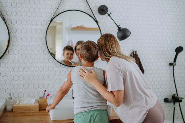 The diabetic boy and his mom getting ready in the morning, while wearing a continuous glucose monitoring sensor on his arm. CGM device making life of school boy easier, helping manage his illness and focus on other activities.