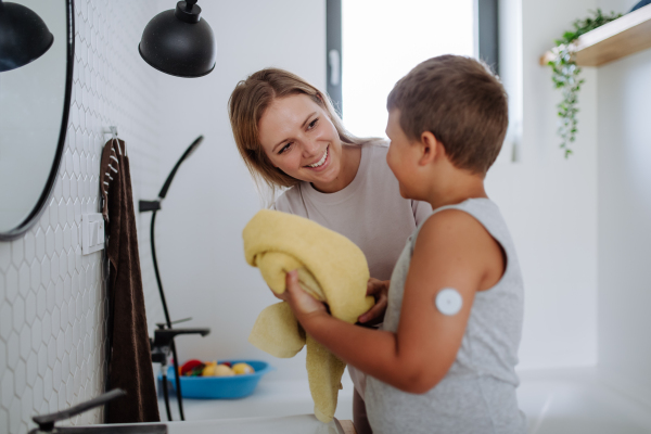 The diabetic boy getting ready in the morning, while wearing a continuous glucose monitoring sensor on his arm. CGM device making life of school boy easier, helping manage his illness and focus on other activities.