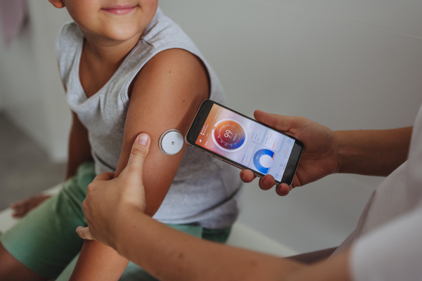 Boy with diabetes checking blood glucose level at home using continuous glucose monitor. The boy's mother connects his CGM to a smartphone to monitor his blood sugar levels in real time.