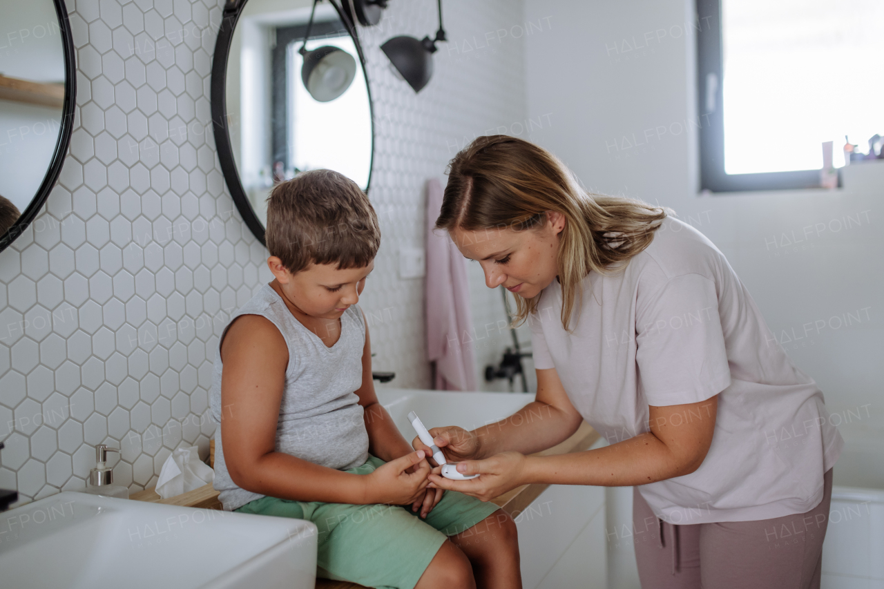 Mother checking her son's blood glucose level at home using a fingerstick glucose meter. The diabetic boy with blood on his fingertip, waiting to analyze his current blood sugar level.