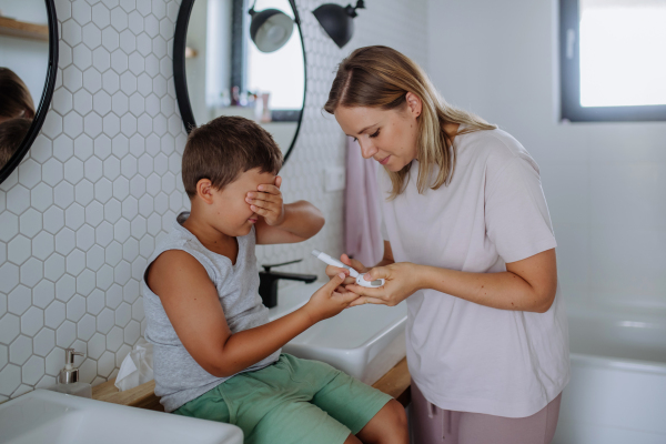 Mother checking her son's blood glucose level at home using a fingerstick glucose meter. The diabetic boy can't watch as his mother pricks his skin to obtain a blood sample.