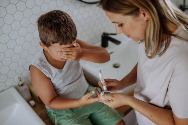 Mother checking her son's blood glucose level at home using a fingerstick glucose meter. The diabetic boy waiting for results from his blood test. Mother caressing her son's cheek.