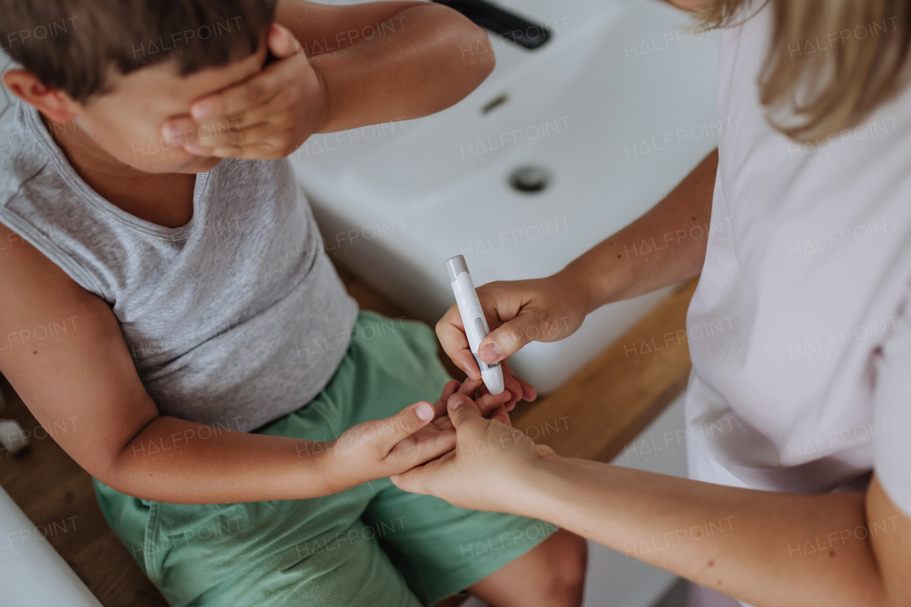 Mother checking her son's blood glucose level at home using a fingerstick glucose meter. The diabetic boy can't watch as his mother pricks his skin to obtain a blood sample.