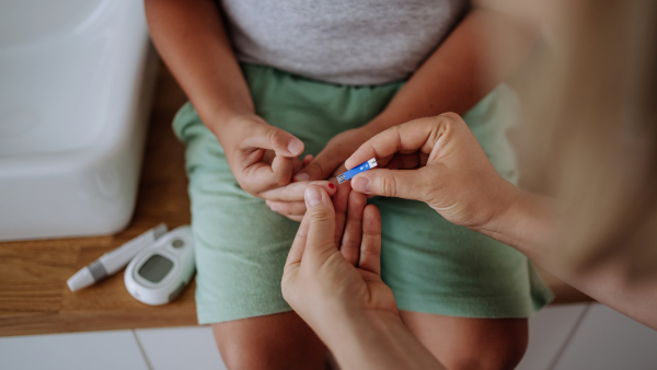 Mother checking her son's blood glucose level at home using a fingerstick glucose meter. The diabetic boy waiting for results from his blood test. Mother caressing her son's cheek.