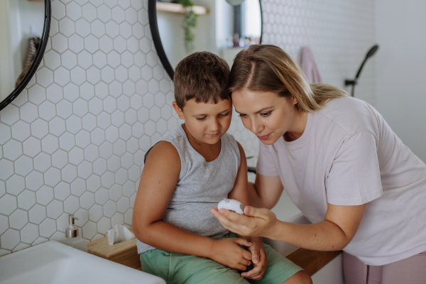 Mother checking her son's blood glucose level at home using a fingerstick glucose meter. The diabetic boy waiting for results from his blood test.