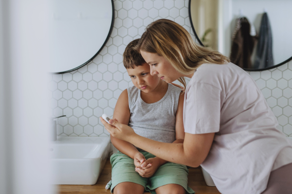 Mother checking her son's blood glucose level at home using a fingerstick glucose meter. The diabetic boy waiting for results from his blood test. Mother caressing her son's cheek.