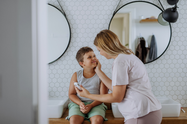 Mother checking her son's blood glucose level at home using a fingerstick glucose meter. The diabetic boy waiting for results from his blood test. Mother caressing her son's cheek.