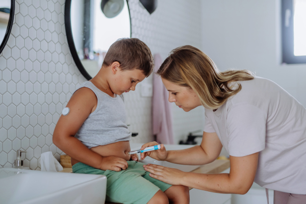 Mother of diabetic boy injecting insulin in his belly. Young boy with type 1 diabetes taking insuling with syringe needle in bathroom..