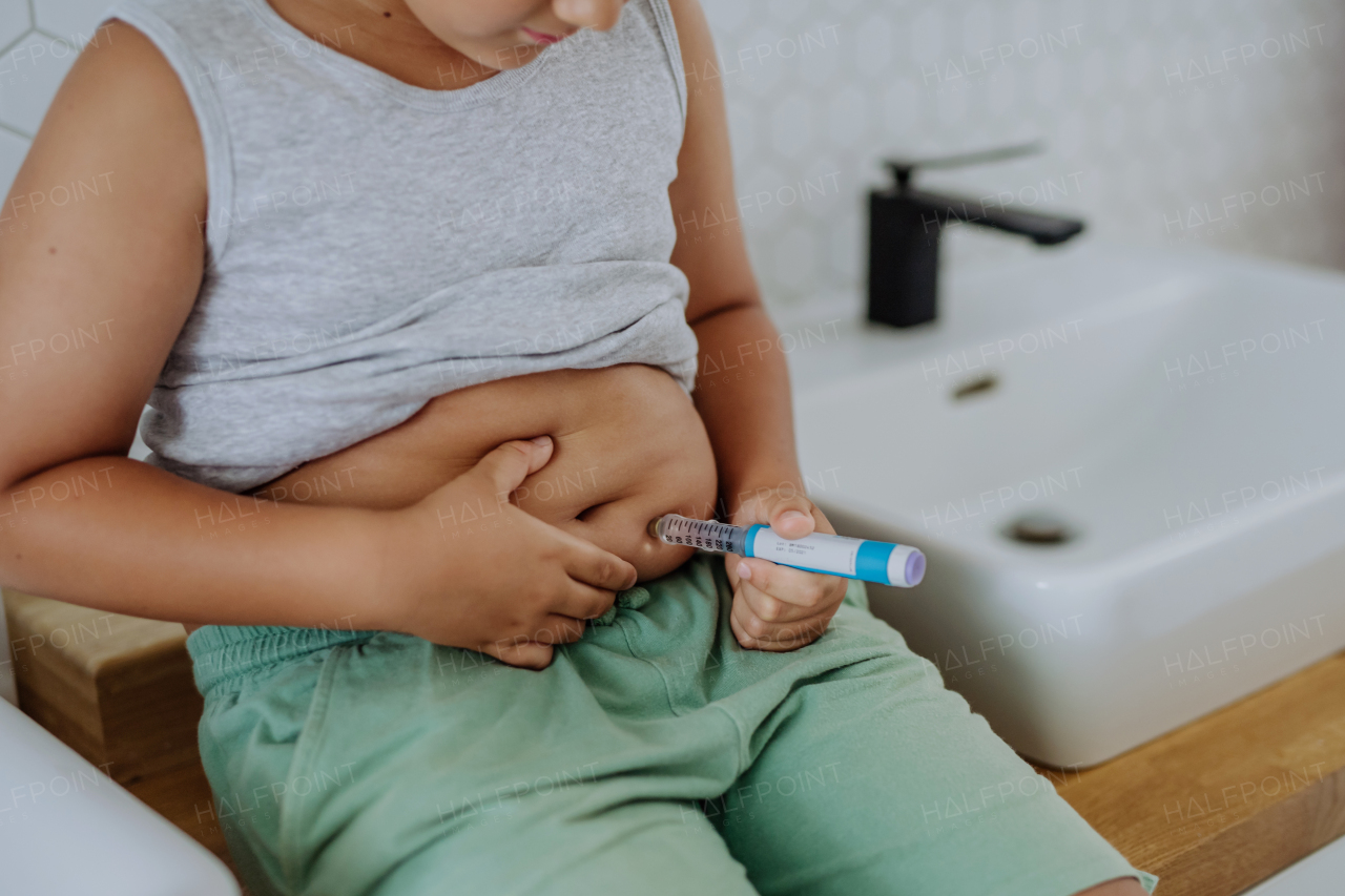 Little boy with diabetes injecting insulin in his belly. Close up of young boy with type 1 diabetes taking insuling with syringe needle.