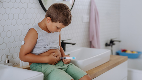 Little boy with diabetes injecting insulin in his belly. Close up of young boy with type 1 diabetes taking insuling with syringe needle.